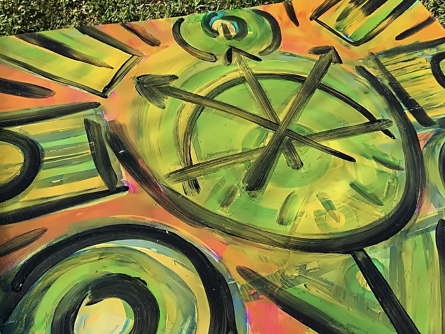 Detalhe de um quadro em laranja e verde, com uma grande roda de raios cruzados em preto e formas curvas.