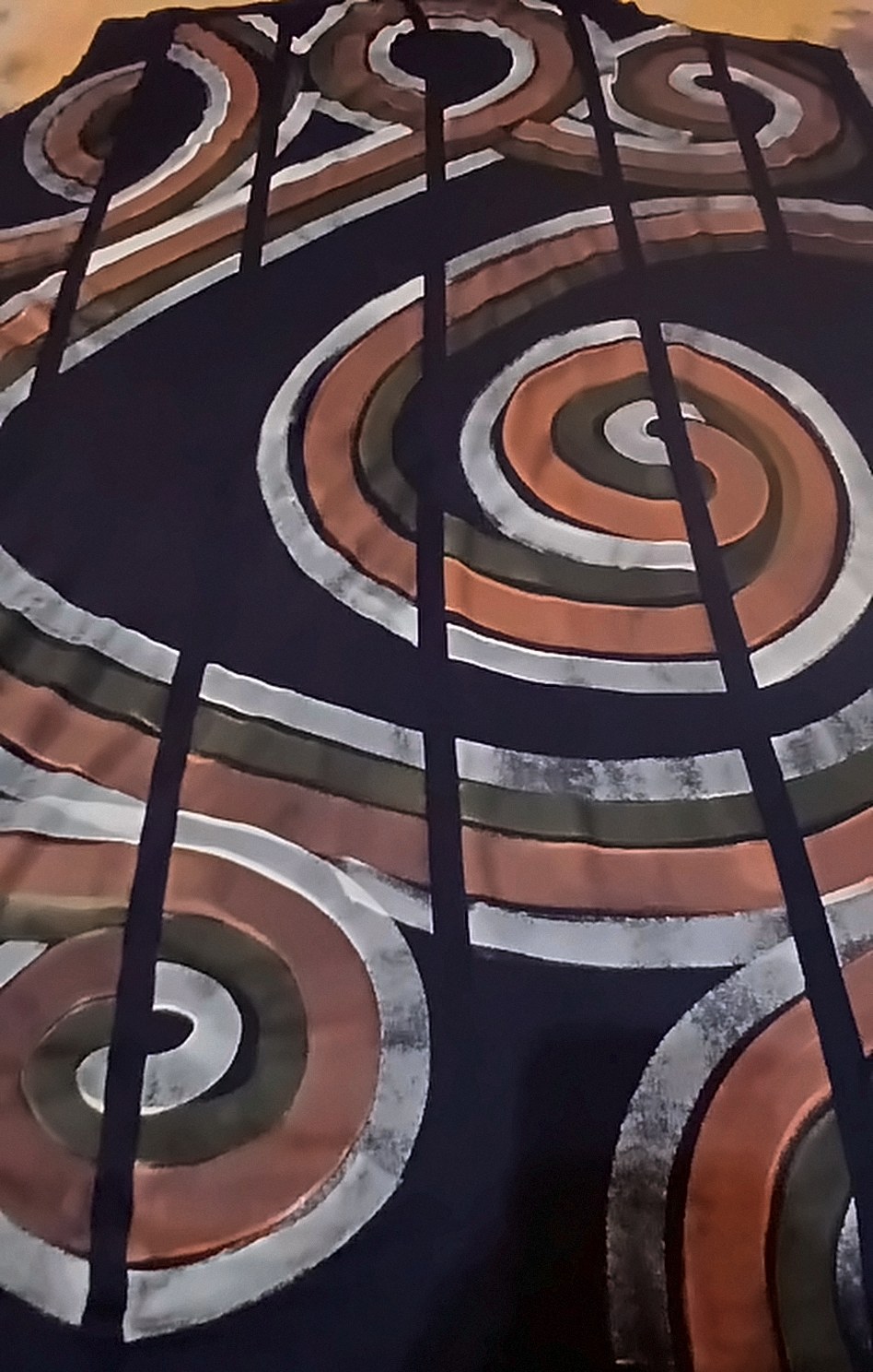 Tecido preto esticado sobre a mesa, com espirais pintadas à mão em cobre, verde-oliva e prata.