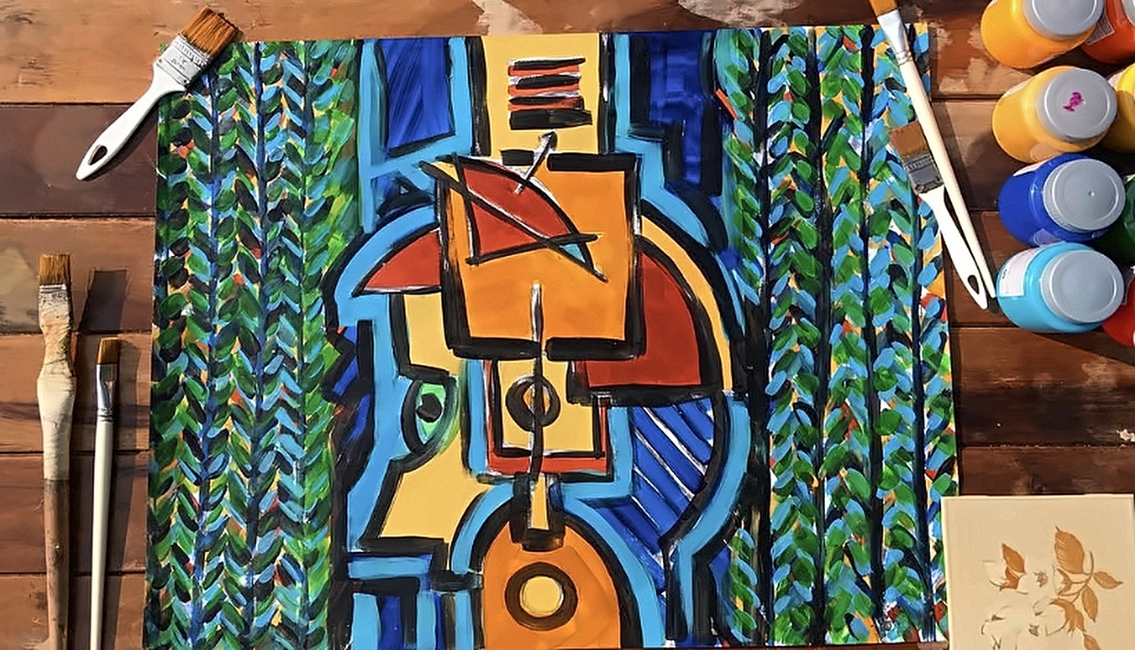 Pintura de formas geométricas em azul, laranja, vermelho e preto, entre faixas de folhas verdes, sobre uma mesa de madeira com pincéis e potes de tinta.